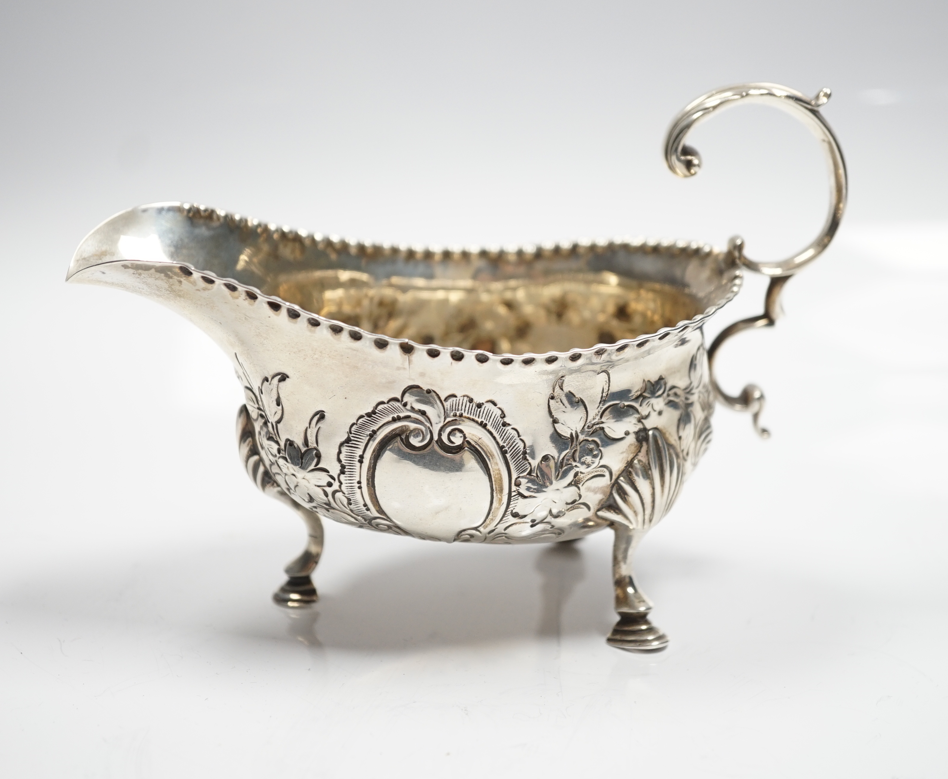 A George III silver sauce boat, with flying scroll handled and later embossed decoration, maker T?, London, 1776, length 15.5cm, 5.75oz.